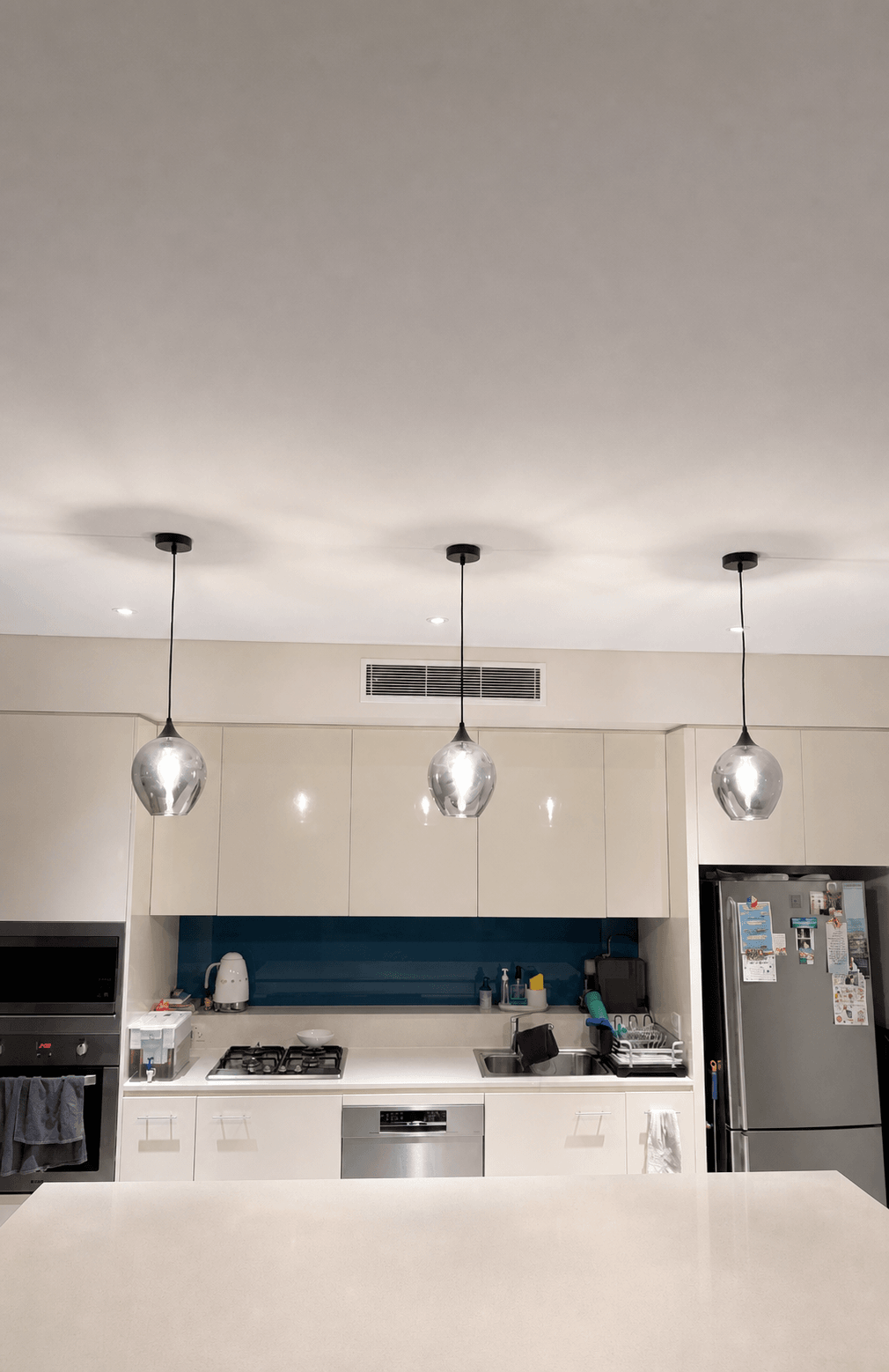 Three pendant lights installed above a residential kitchen bench